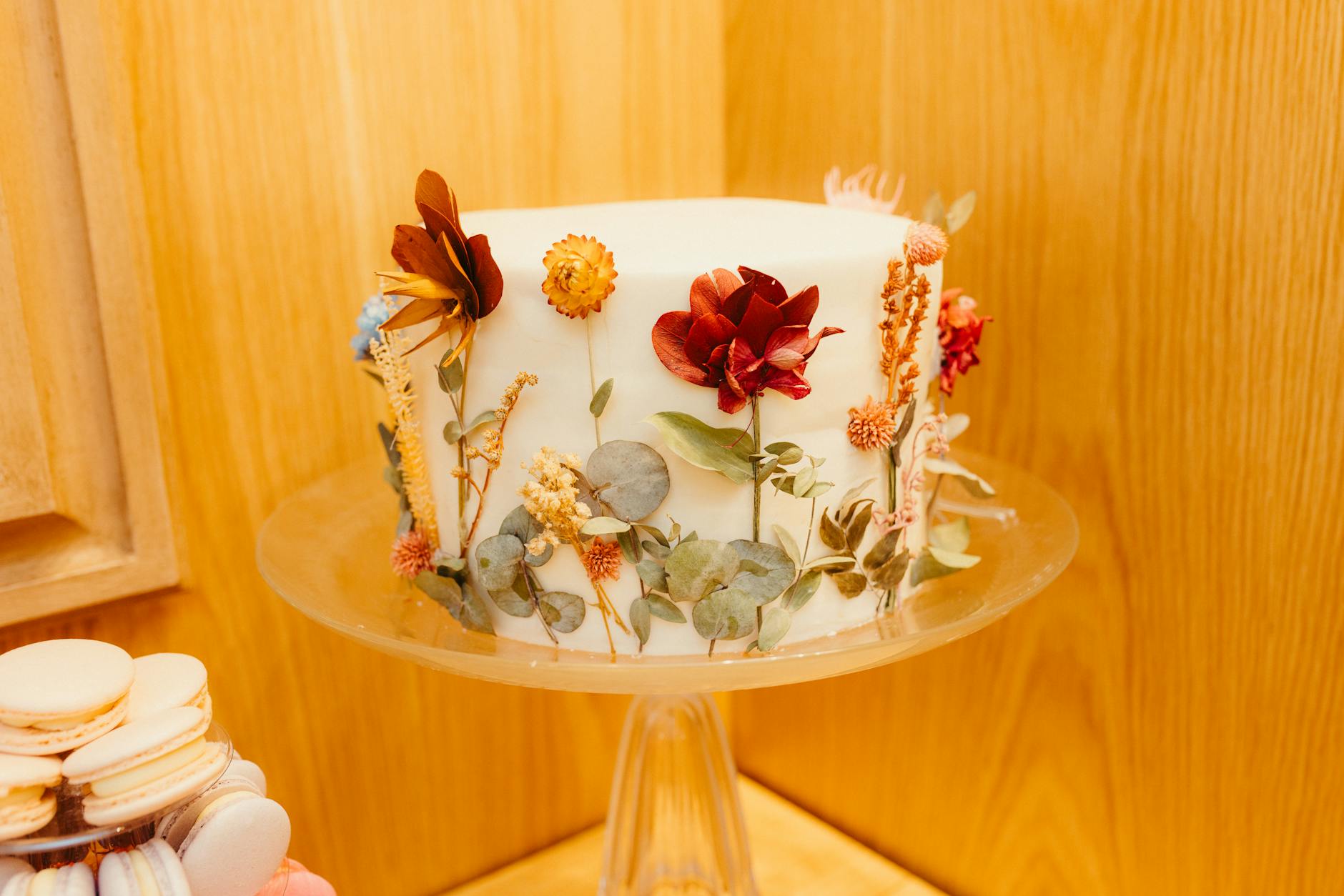 Biały tort na szklanej paterze udekorowany jadalnymi kwiatami