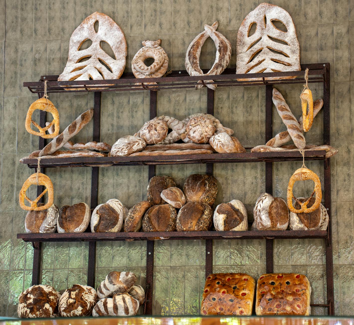 Co zrobić z czerstwym pieczywem: grzanki, tarte bułki i roślinne zapiekanki Bochny rzemieślniczego pieczywa ułożone na drewnianych półkach