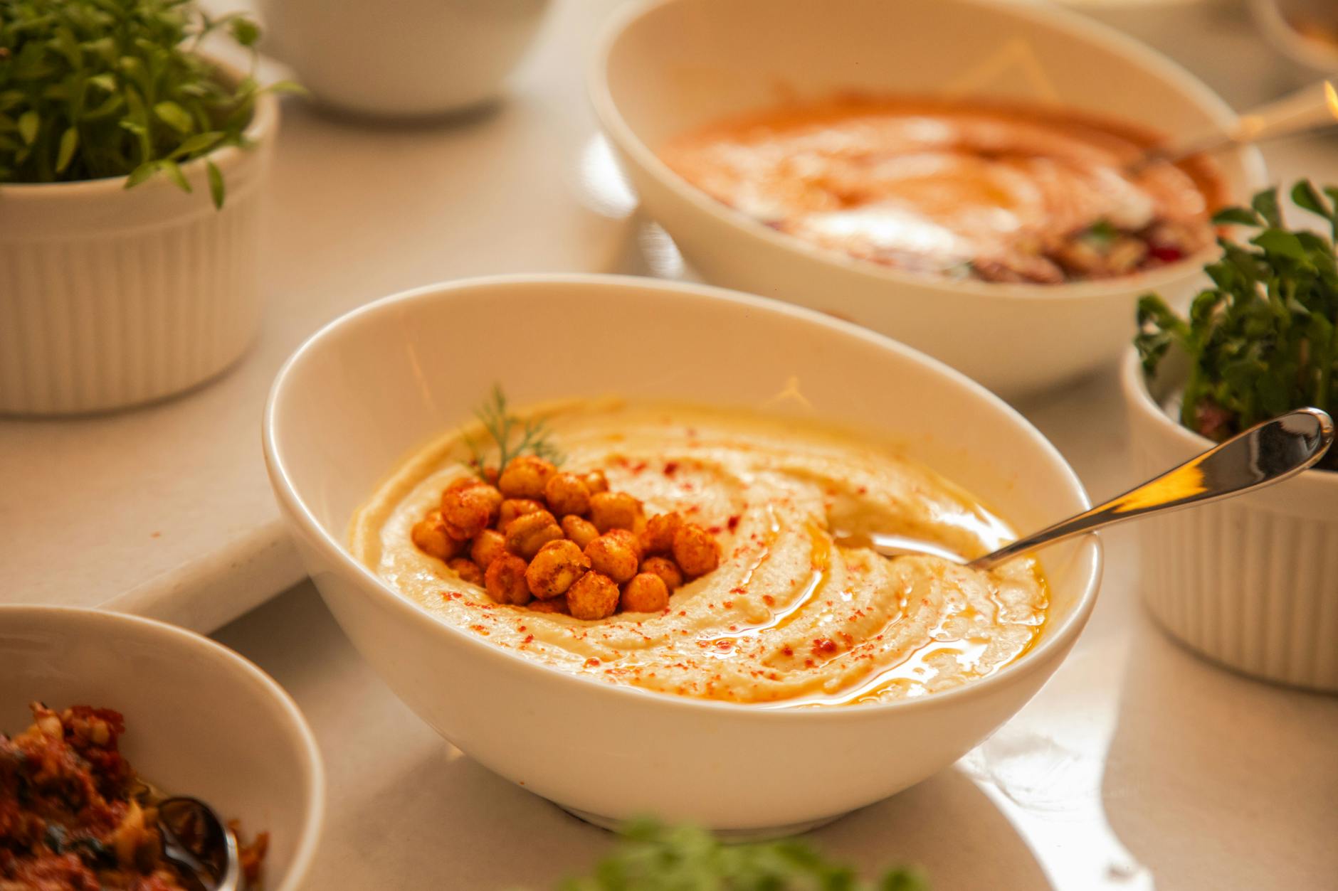 Jak zrobić idealny hummus: wybór ciecierzycy, tahini i trik na jedwabistą konsystencję Miska kremowego hummusu z ciecierzycą i ziołami z bliska